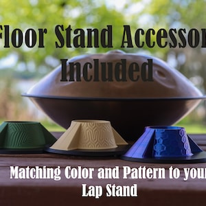 May include: A brown steel tongue drum sits behind three conical stands in green, beige, and blue, each featuring distinct geometric patterns. Text reads: Floor Stand Accessory Included. Matching Color and Pattern to your Lap Stand.