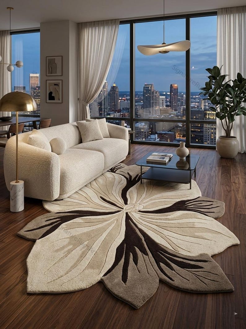 May include: A large, petal-shaped area rug featuring a central floral design in shades of cream, beige, and dark brown. The rug has a textured, tufted surface with organic, curved lines radiating from the center, mimicking the appearance of a flower.