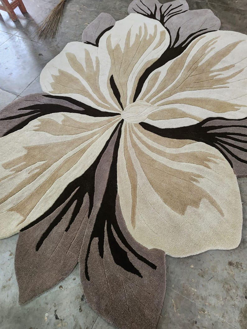 May include: A large, flower-shaped area rug featuring a layered petal design in shades of cream, beige, taupe, and dark brown. The rug has a textured, tufted surface with distinct color blocking that defines the organic, curved shapes of the petals.