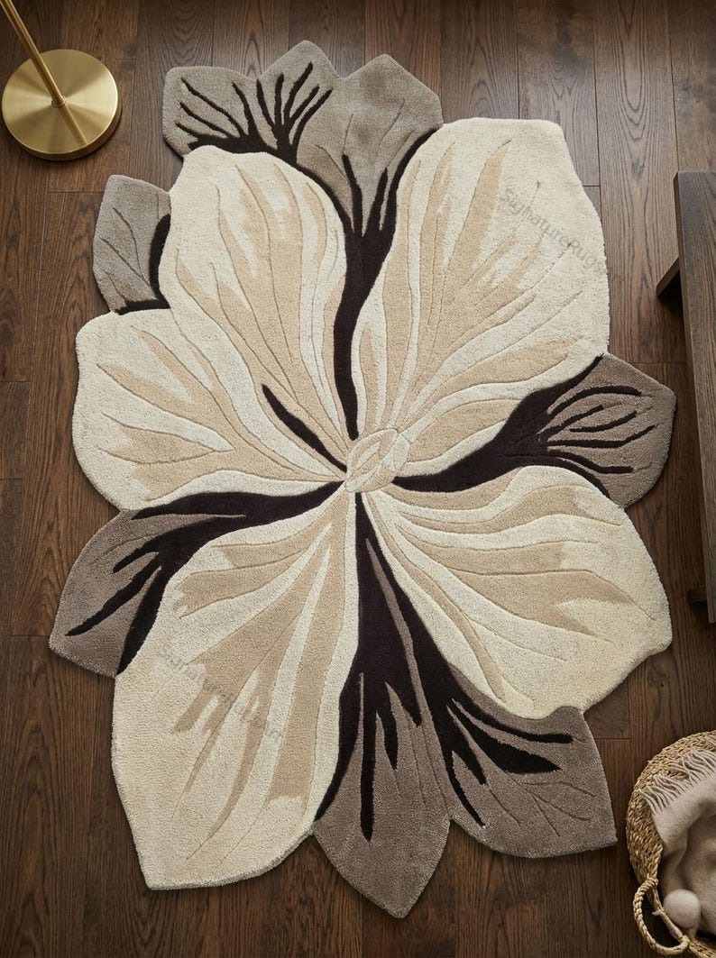 May include: A tufted area rug shaped like a large flower with organic, irregular edges. The design features a color palette of cream, beige, and dark brown, with deep brown accents radiating from the center to define the petal-like segments.