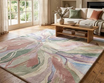 May include: A large, rectangular area rug with an abstract design in pastel colors. The rug features a blend of pink, green, purple, and blue hues, creating a soft, flowing pattern. It's placed on a hardwood floor in a living room setting.