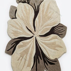 May include: A tufted rug shaped like a large flower with irregular, organic petals. The design features a color palette of cream, beige, and dark brown, with deep brown lines radiating from the center. The text SignatureRugsArt is visible.