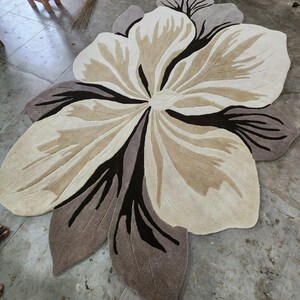 May include: A large, flower-shaped area rug featuring a layered petal design in shades of cream, beige, taupe, and dark brown. The rug has a tufted texture with distinct color blocking that defines the organic, curved edges of the floral motif.