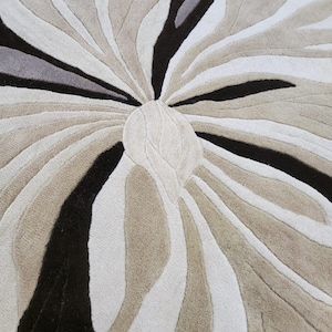 May include: A tufted area rug featuring a large, abstract floral-inspired pattern. The design consists of radiating, organic shapes in shades of cream, beige, dark brown, and grey, with deep pile textures creating a high-contrast, layered appearance.