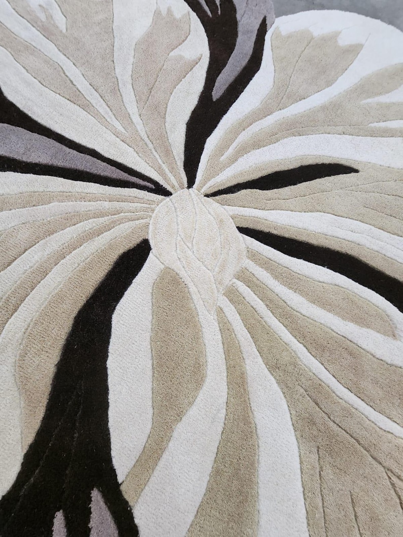 May include: A tufted area rug featuring a large, abstract floral-inspired pattern. The design consists of radiating, organic shapes in shades of cream, beige, dark brown, and grey, with deep pile textures creating a high-contrast, layered appearance.