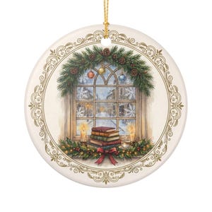 May include: A round ceramic ornament featuring a festive illustration of a window overlooking a snowy street. The scene includes a stack of books, two lit candles, a teacup, and a pine garland with ornaments, all framed by an ornate gold border.