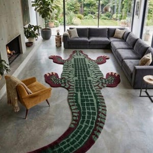 May include: A large, floor-covering rug shaped like an alligator, featuring a textured surface with a dark green and light green scale pattern, bordered by a deep maroon edge, with four splayed legs and a long, curved tail extending across the floor.