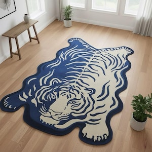 Op de afbeelding: Een marineblauwe en crèmekleurige tapijt in de vorm van een tijger. Het tapijt toont een tijger met strepen en een golvende rand. Het tapijt ligt op een houten vloer. Afmetingen: ongeveer 180 cm.