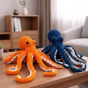 Könnte beinhalten: Zwei gehäkelte Oktopus-Plüschtiere. Einer ist leuchtend orange mit weißen Akzenten an seinen Tentakeln, der andere ist tiefblau mit weißen Akzenten. Beide haben schwarze Augen und werden auf einem Holztisch präsentiert.