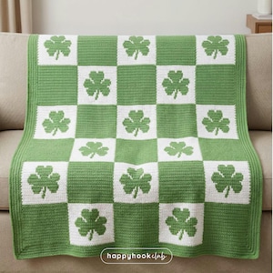 Può includere: Una coperta all'uncinetto verde e bianca con un motivo a scacchiera. Ogni quadrato bianco presenta un trifoglio verde. La coperta è drappeggiata su un divano beige. Le parole "happyhookclub" sono visibili in basso a destra.