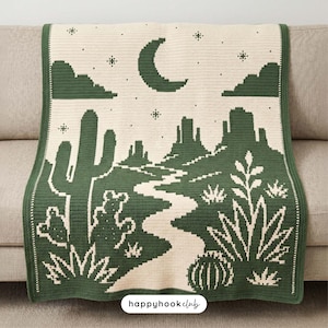 Puede incluir: Una manta de ganchillo rectangular con un diseño de paisaje desértico en verde oscuro y crema. El patrón muestra una luna creciente, estrellas, nubes, cactus y un camino sinuoso. El texto "happyhookclub" está impreso en negro en el centro.