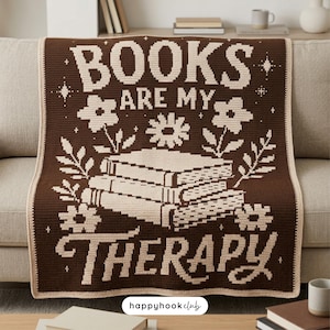 Può includere: Una coperta all'uncinetto marrone e crema con la scritta "BOOKS ARE MY THERAPY" e una pila di libri, fiori e foglie. La coperta è drappeggiata su un divano. Un elemento d'arredo per la casa.