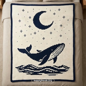 May include: A cream-coloured crocheted blanket featuring a navy blue whale leaping from the ocean under a crescent moon and stars. The blanket has a navy blue border and the text "happyhookclub" in the bottom right corner.