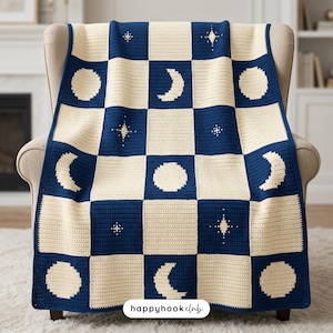 Op de afbeelding: Een gehaakte deken met een hemels thema, met een dambordpatroon van marineblauwe en crèmekleurige vierkanten. Het ontwerp bevat halve manen, sterren en cirkels. De deken is over een beige fauteuil gedrapeerd.