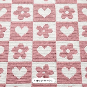May include: A crocheted blanket with a repeating pattern of pink squares alternating with white squares. The white squares feature either a heart or a flower design. The words "happyhookclub" are in the bottom right corner.