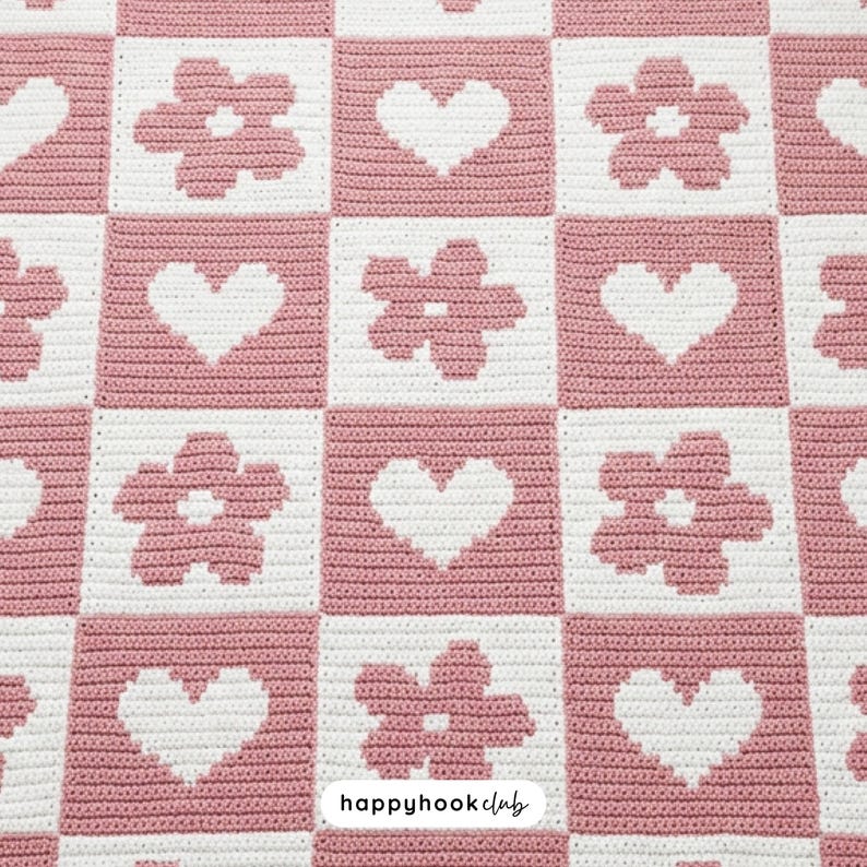 May include: A crocheted blanket with a repeating pattern of pink squares alternating with white squares. The white squares feature either a heart or a flower design. The words "happyhookclub" are in the bottom right corner.