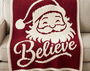May include: A deep red and cream crochet blanket featuring a large graphic of Santa Claus wearing a hat and the word Believe written in a cursive script below the face. The blanket has a cream-colored border and a small white tag at the bottom.