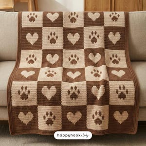 May include: A brown and cream crochet blanket featuring a checkerboard design with paw prints and hearts. The blanket is displayed on a sofa. The text "happyhookclub" is visible at the bottom.
