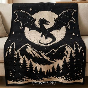 May include: Black and beige crochet blanket featuring a dragon design. The blanket depicts a dragon in front of a full moon, with mountains and trees at the bottom. The blanket is draped over a sofa.