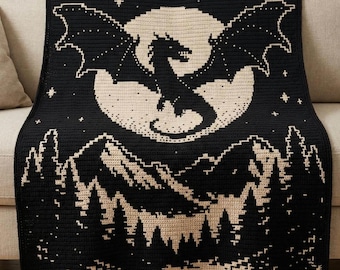 Puede incluir: Manta de ganchillo negra y beige con un diseño de dragón. La manta representa un dragón frente a una luna llena, con montañas y árboles en la parte inferior. La manta está sobre un sofá.