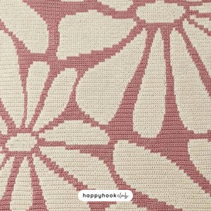 May include: Close-up of a crocheted blanket with a large floral pattern. The design features white flower petals outlined and filled with a dusty rose color against a cream-colored background. The text "happyhookclub" is in the bottom right corner.