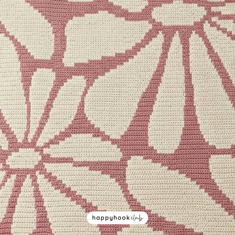 May include: Close-up of a crocheted blanket with a large floral pattern. The design features white flower petals outlined and filled with a dusty rose color against a cream-colored background. The text "happyhookclub" is in the bottom right corner.
