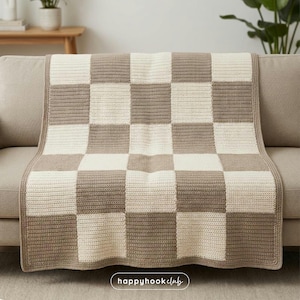 May include: A beige and cream-colored crocheted blanket with a checkerboard pattern. The blanket is draped over a beige sofa. The text "happyhookclub" is in the bottom right corner.