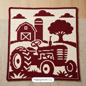 May include: A rectangular crochet blanket featuring a two-tone farm scene in dark red and cream. The design displays a tractor in the foreground, with a barn, silo, tree, and clouds in the background. The text "happyhookclub" is printed at the bottom.