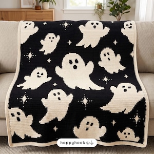 Puede incluir: Una manta de ganchillo negra y crema con un patrón repetitivo de varios fantasmas y pequeñas estrellas de cuatro puntas. La manta tiene un borde liso de color crema y una etiqueta rectangular blanca con el texto happyhookclub en el centro.