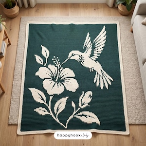 Puede incluir: Una manta de ganchillo rectangular con fondo verde bosque oscuro y un diseño en color crema de un colibrí sobrevolando una gran flor de hibisco y un capullo. La manta tiene un borde color crema y el texto happyhookclub.