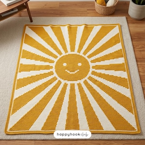 May include: A yellow and white crochet blanket featuring a smiling sun design. The sun's face is in the center, with radiating stripes. The blanket is rectangular and appears to be handmade. The text "happyhook club" is in the bottom right corner.