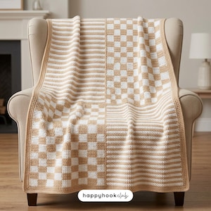 May include: A handmade crochet blanket in cream and tan, draped over a beige armchair. The blanket features a checkerboard and striped pattern. The blanket is a cozy home decor item.