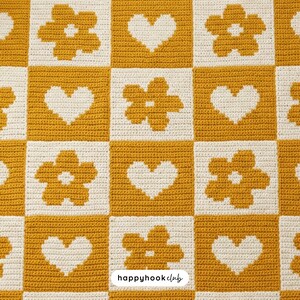May include: A crocheted blanket with a checkerboard pattern. Alternating squares of mustard yellow and cream. The yellow squares feature white heart and flower designs. The text "happyhook club" is in the bottom right corner.