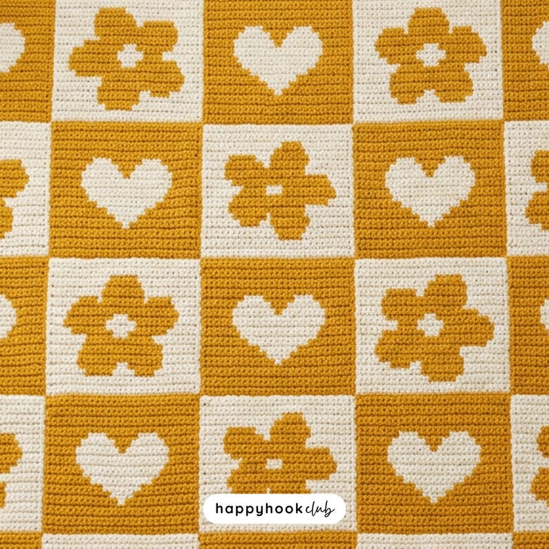May include: A crocheted blanket with a checkerboard pattern. Alternating squares of mustard yellow and cream. The yellow squares feature white heart and flower designs. The text "happyhook club" is in the bottom right corner.