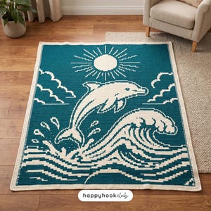May include: A rectangular crochet blanket featuring a teal background with a white pixelated design of a dolphin leaping over ocean waves under a sun and clouds. The text "happyhookclub" is printed in black on a white label at the bottom center.