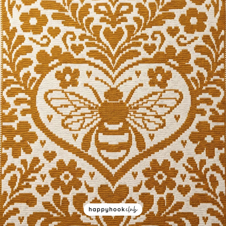 May include: A mustard yellow and off-white crocheted textile featuring a central bee motif enclosed within a heart shape, surrounded by symmetrical floral and leaf patterns. The bottom center includes a white label with the text happyhookclub.