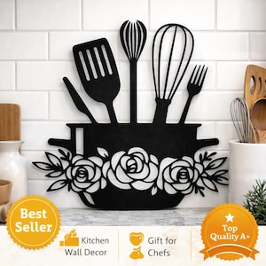 Op de afbeelding: Zwarte metalen keukenwanddecoratie met een potvorm met rozen en keukengerei. Het ontwerp omvat een spatel, garde, vork en lepel. De woorden "Best Seller", "Kitchen Wall Decor", "Gift for Chefs" en "Top Quality A+" zijn ook zichtbaar.