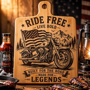 May include: A wooden chopping board featuring a motorcycle and an American flag. The board is engraved with the words "RIDE FREE - LIVE BOLD" and "BUILT FOR THE ROAD - MADE FOR LEGENDS". A bottle of BBQ sauce and a cast iron pan are in the foreground.