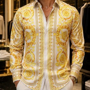Pode incluir: Uma camisa branca de manga comprida com um padrão barroco dourado. A camisa é combinada com calças brancas. O design da camisa apresenta motivos florais e de rolagem ornamentados.