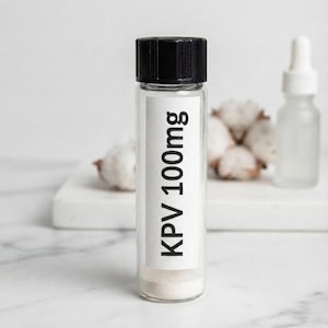 Peut inclure: Un flacon en verre transparent avec un bouchon à vis noir contenant une poudre blanche. Une étiquette rectangulaire blanche est apposée sur le devant du flacon avec le texte imprimé en noir KPV 100mg. Le flacon est cylindrique et transparent.
