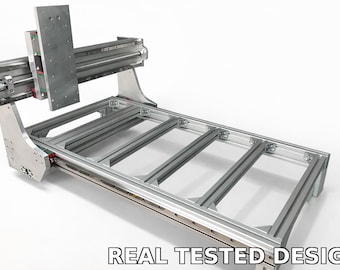 May include: A silver CNC machine with a rectangular frame and a gantry system. The machine has a series of parallel rails and a vertical support structure. The text "REAL TESTED DESIGN" is displayed at the bottom.