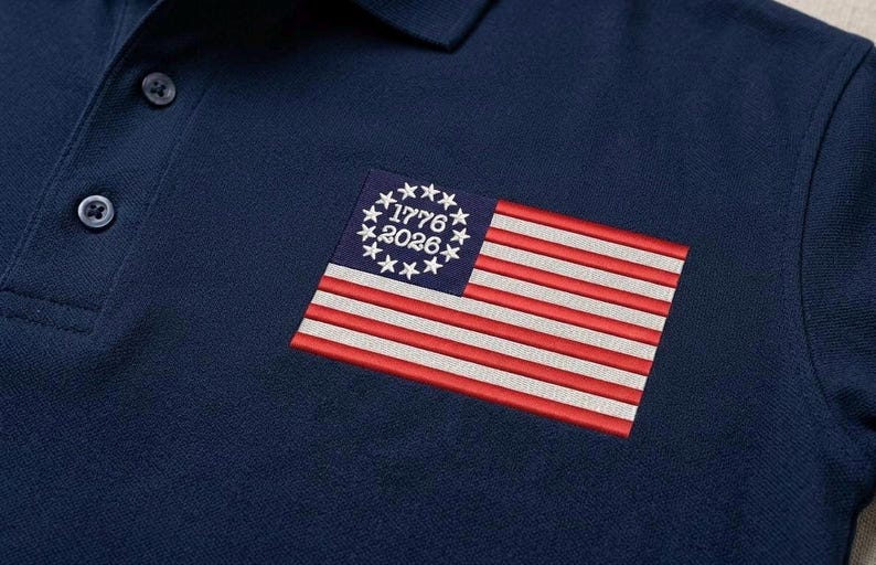 May include: Navy blue polo shirt with a small embroidered American flag patch. The flag features red and white stripes, a blue field with stars, and the dates "1776" and "2026". The shirt has a classic collar and button placket.