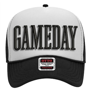 Puede incluir: Gorra de camionero en blanco y negro con la palabra "GAMEDAY" en letras negras grandes y en negrita en la parte delantera. La gorra tiene un panel frontal blanco, una visera negra y una parte trasera de malla. Un pequeño parche con texto en la parte inferior.