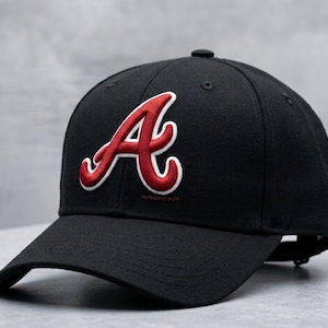 Könnte beinhalten: Schwarze Baseballkappe mit einem rot-weiß gestickten Buchstaben "A" auf der Vorderseite. Die Kappe hat einen gebogenen Schirm und einen kleinen Knopf. Der Text "AUTHENTIC PUFF" steht darunter.