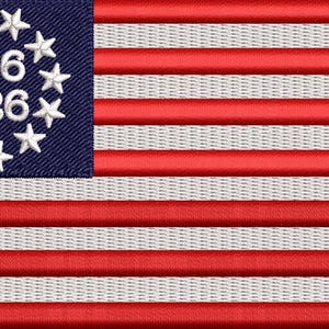 May include: Embroidered flag featuring red and white stripes with a blue canton. The canton displays a circle of white stars surrounding the numbers "1776" and "2026". The flag design is reminiscent of the American flag.