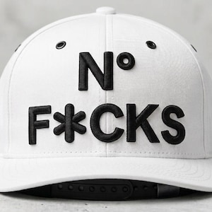 May include: White baseball cap with the text "N° F*CKS" in black, featuring a flat brim and adjustable snapback closure. The hat has a classic six-panel design and a small label on the side.