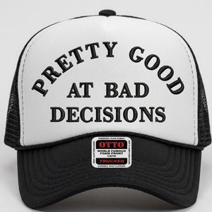 Puede incluir: Gorra de camionero en blanco y negro con el texto "PRETTY GOOD AT BAD DECISIONS" en letras negras en negrita. La gorra tiene una parte delantera de espuma blanca y una parte trasera de malla negra. También tiene un pequeño parche que dice "OTTO" y "TRUCKER".