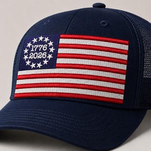 May include: Navy blue baseball cap featuring a patch with the American flag design. The flag includes red and white stripes, a blue field with stars, and the dates "1776" and "2026". The cap has a mesh back.