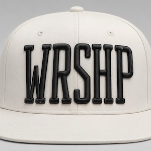 以下が含まれることがあります： フロントパネルに太字の盛り上がった黒い刺繍で「WRSHP」という文字が施されたオフホワイトのベースボールキャップ。この帽子は構造化されたクラウン、フラットなつば、そしてクラウンの中央上部に同素材のボタンが付いています。