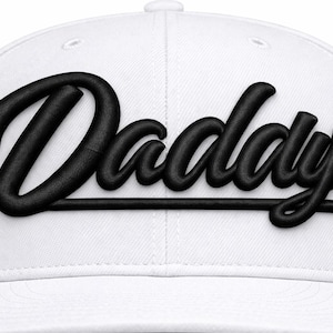 Könnte beinhalten: Weißes Baseball-Cap mit dem Wort "Daddy" in großen, schwarzen, kursiven Buchstaben gestickt. Die Kappe hat einen gebogenen Schirm und einen Knopf oben. Ein modisches Accessoire.